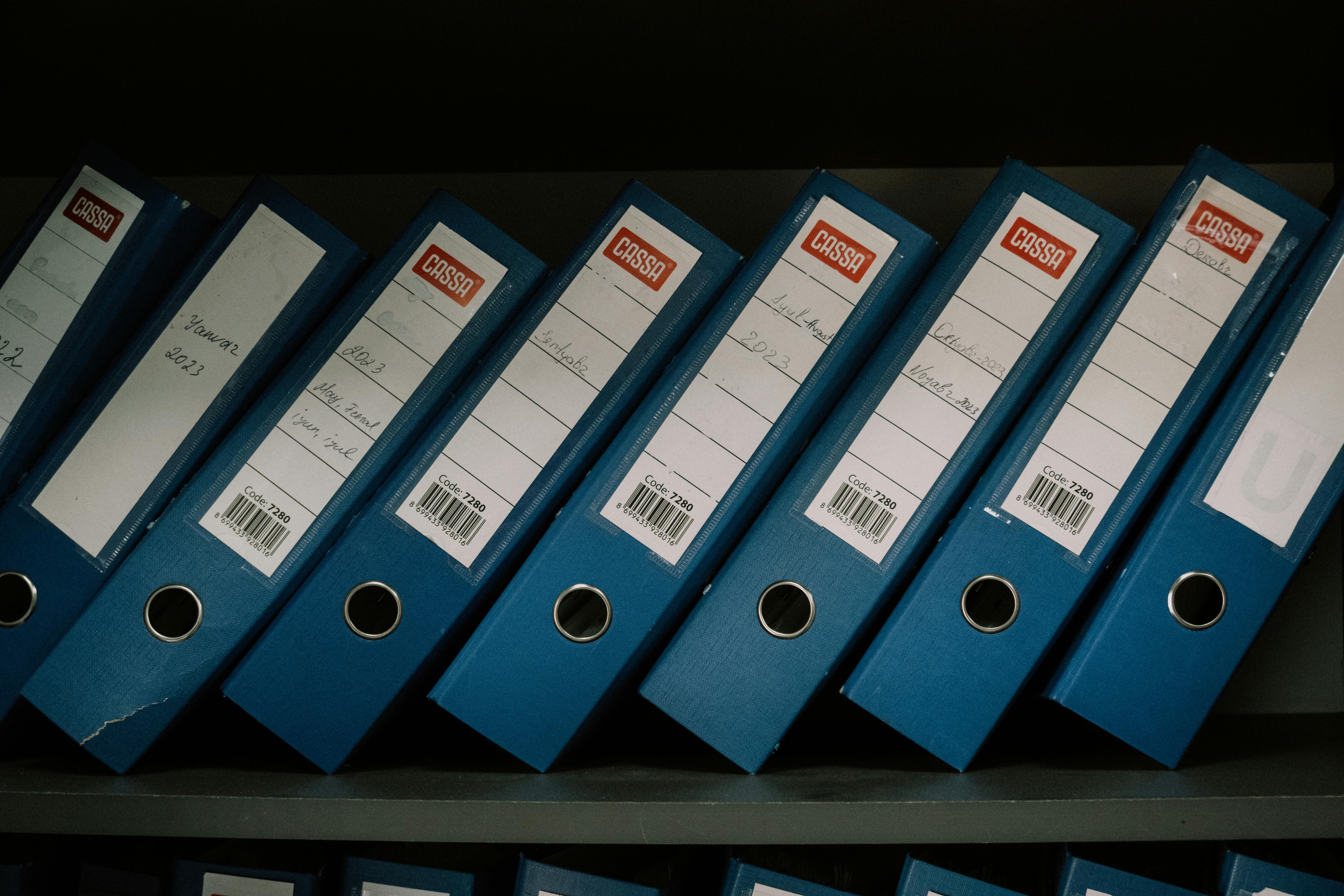 Neatly arranged blue office binders labeled with dates and names for organized storage.